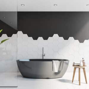 Baignoire îlot noire moderne dans une salle de bain avec carrelage hexagonal blanc et mur supérieur gris foncé, ambiance épurée.