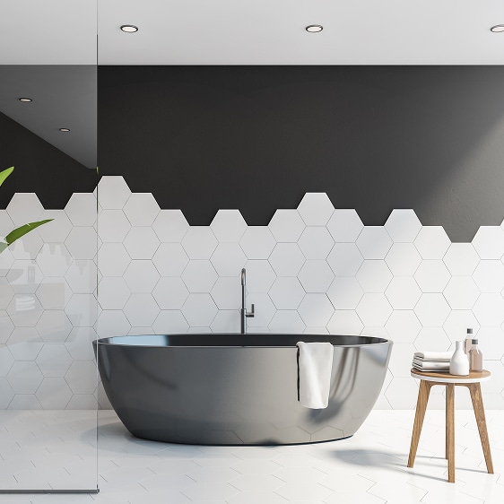 Baignoire îlot noire moderne dans une salle de bain avec carrelage hexagonal blanc et mur supérieur gris foncé, ambiance épurée.