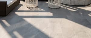 Dalles de sol extérieur grises en grès cérame, éclairées par la lumière du soleil créant des ombres rayées.