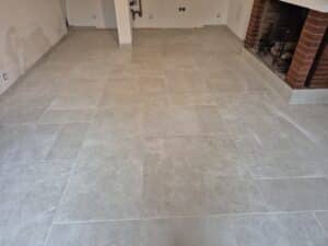 Sol carrelé gris clair de forme rectangulaire dans une pièce en rénovation, avec une cheminée en briques rouges et des murs bruts.