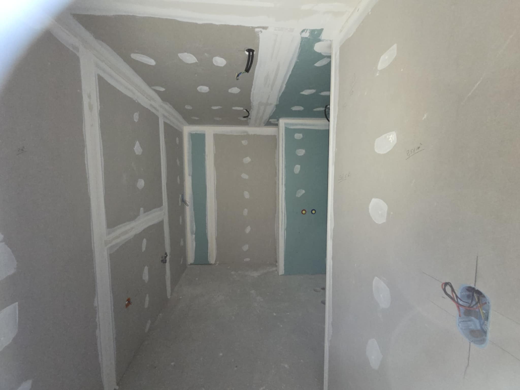 Intérieur en chantier, murs et plafonds en plaques de plâtre (Placo) avec joints enduits, câblage apparent et trous pour prises.