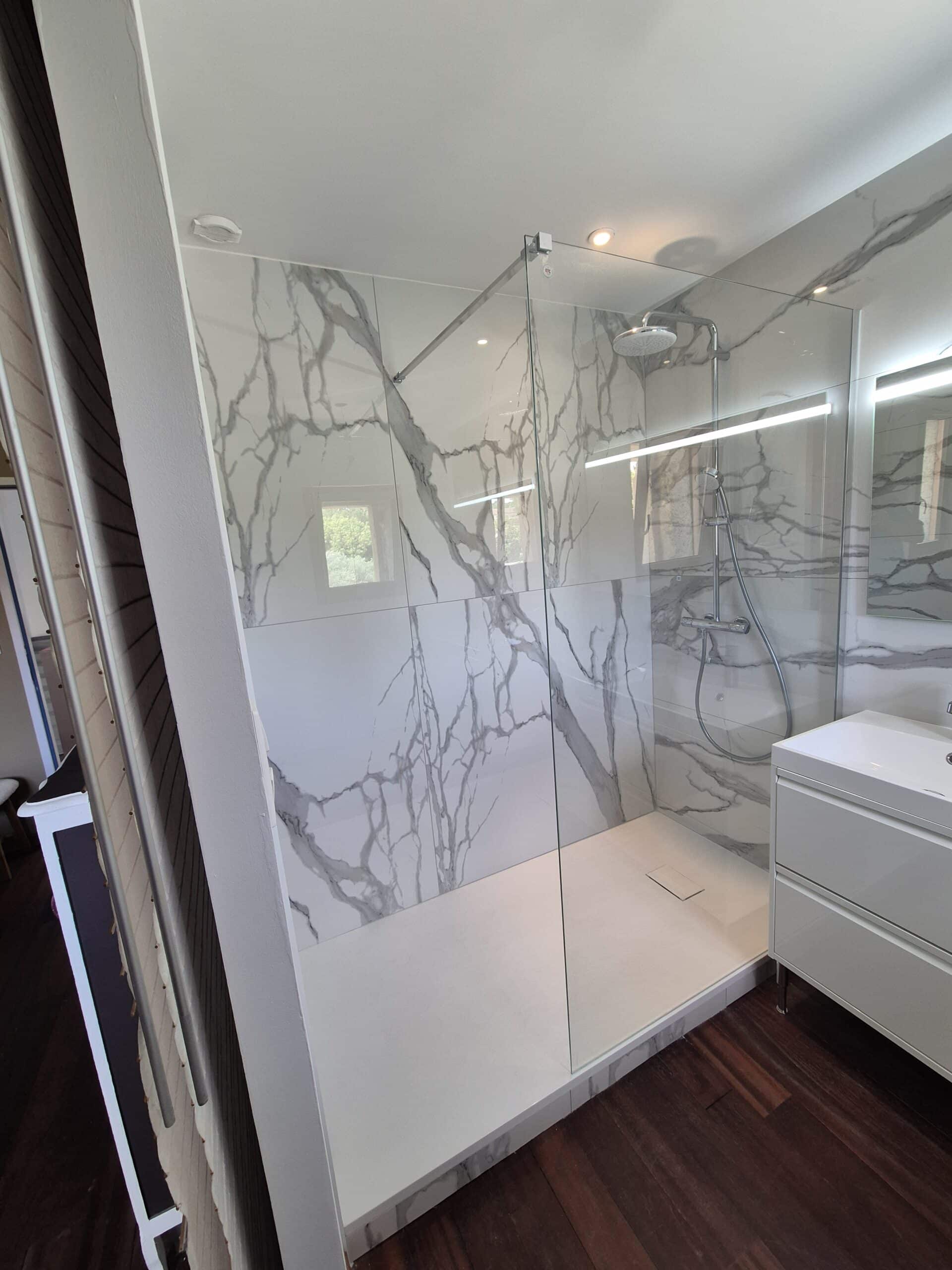 Salle de bain moderne avec douche à l'italienne carrelage effet marbre blanc veiné gris, receveur extra-plat et meuble-lavabo blanc.