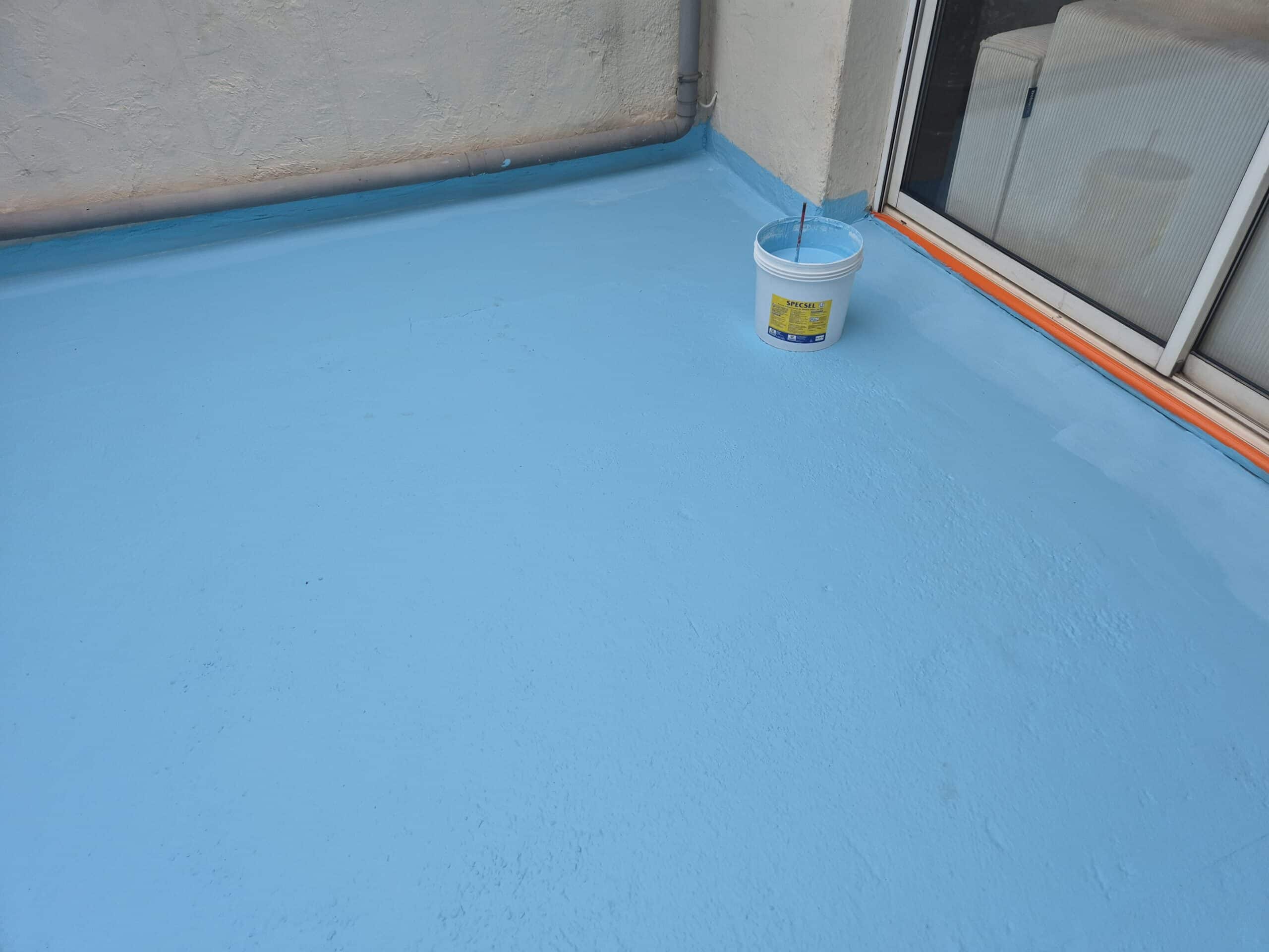 Application d'un revêtement imperméabilisant bleu clair SPECSEL sur une terrasse, près d'une baie vitrée et d'une gouttière.